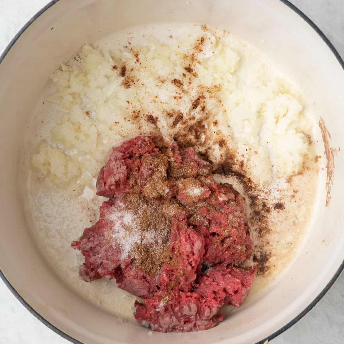 Onions, ground beef and 7 spice in pot before cooking.
