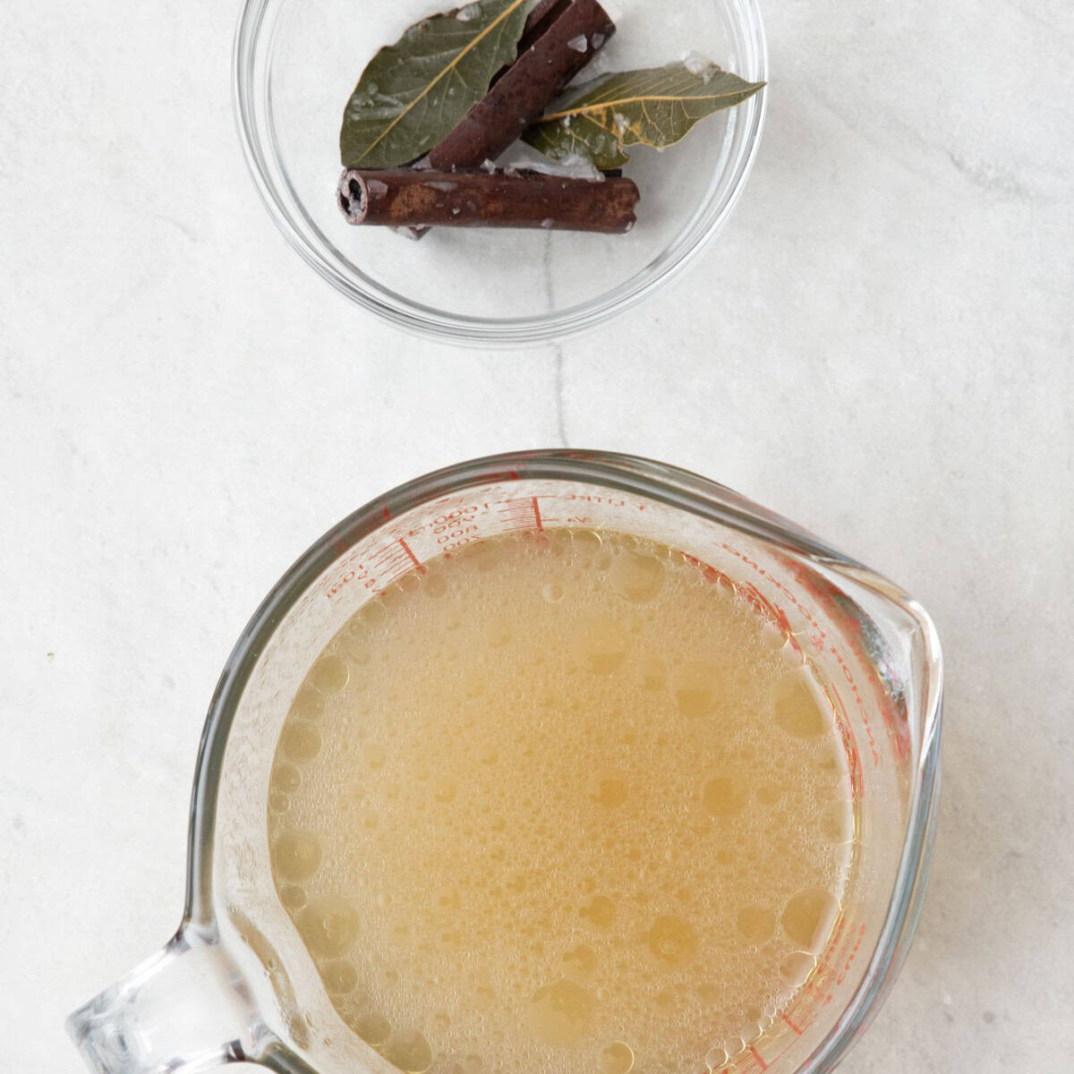 Strained stock in a measuring cup with the removed aromatics sitting in a bowl on the side.