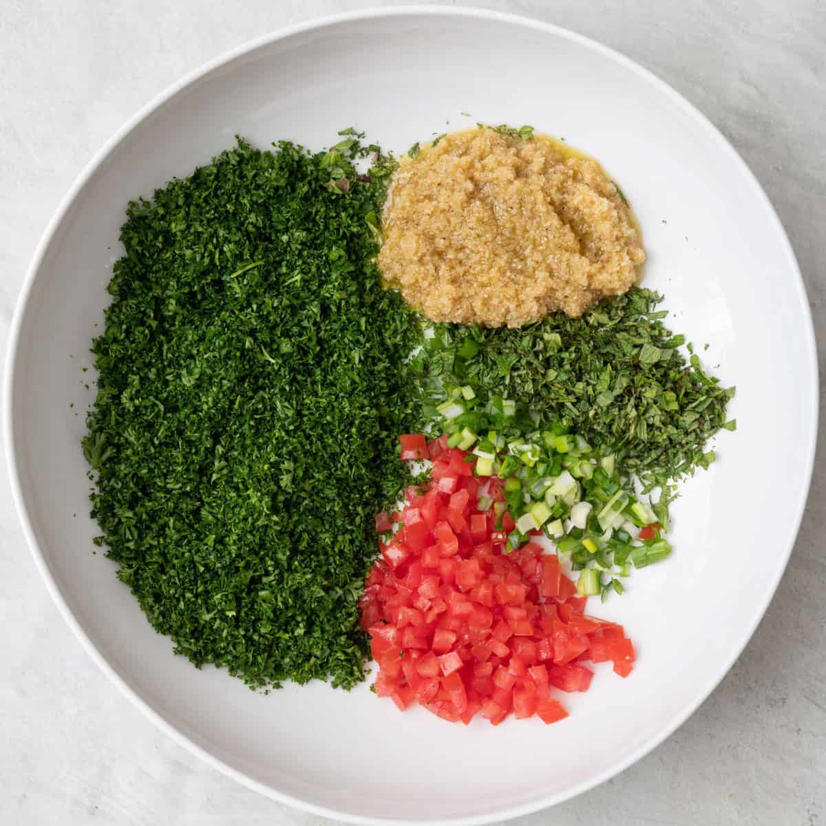 Chopped herbs, tomatoes and bulgur in serving bowl.