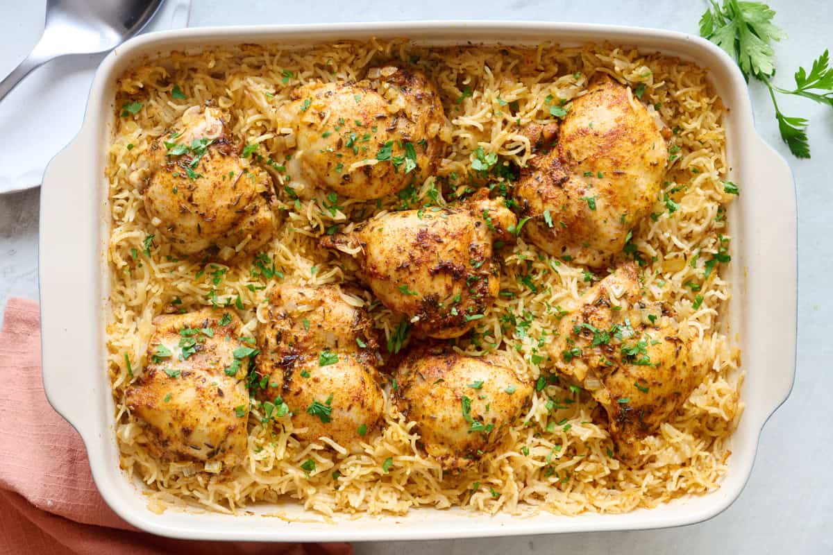 Oven baked chicken thighs and basmati rice in a baking dish garnished with fresh parsley.