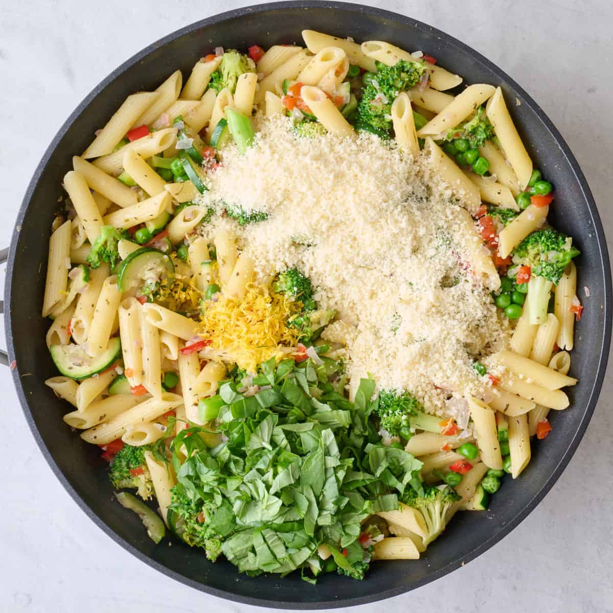 Parmesan and chopped basil added to recipe in pan.