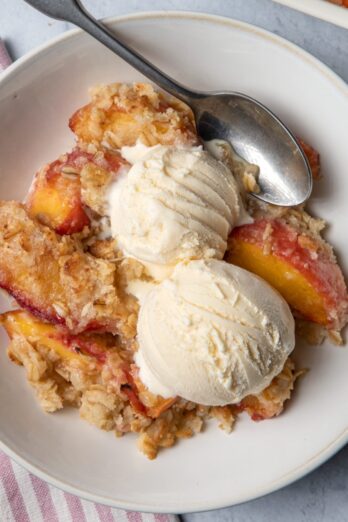 Peach crisp in a bowl served with two scoops of vanilla ice cream