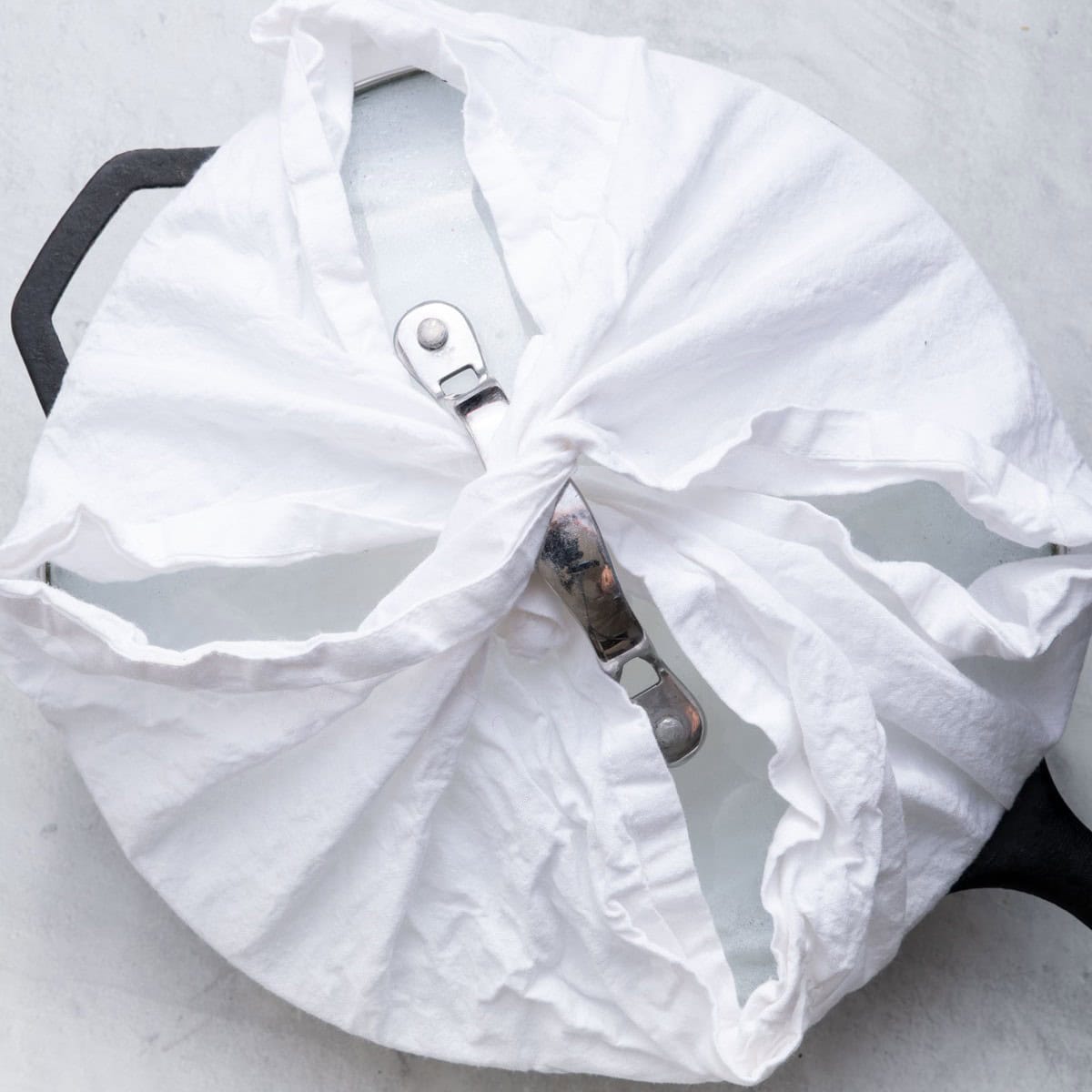 Cast iron skillet covered with lid wrapped with clean towel.