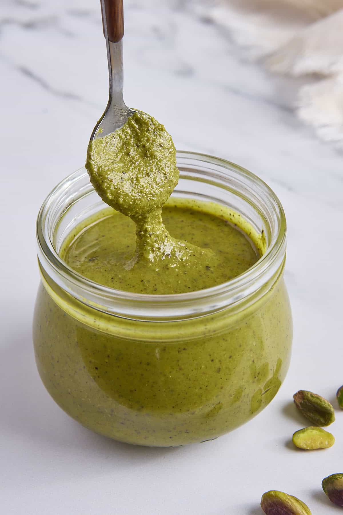 Jar with spoon lifting some pistachio butter up and it drizzling back inside jar.