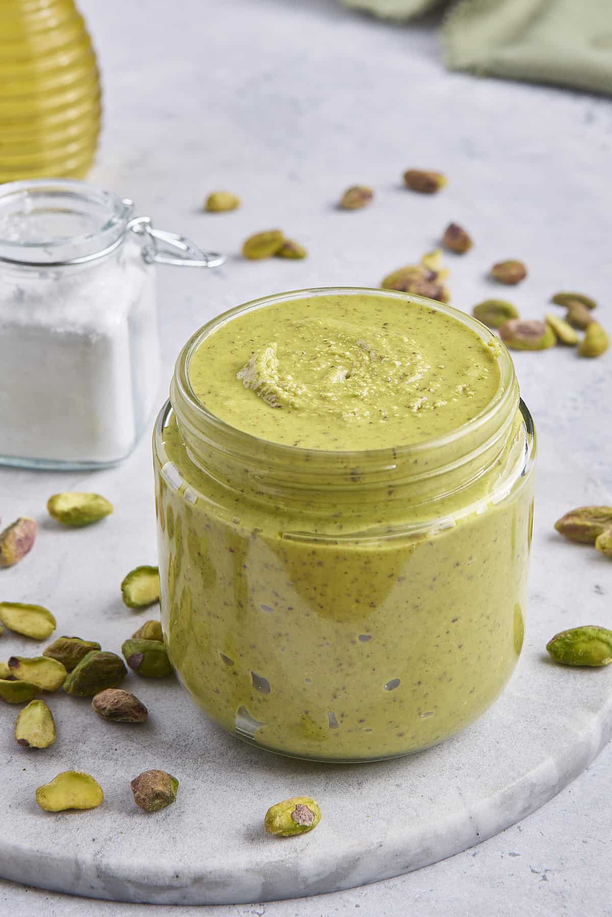 Homemade pistachio cream in a small class jar with extra shelled pistachios around.