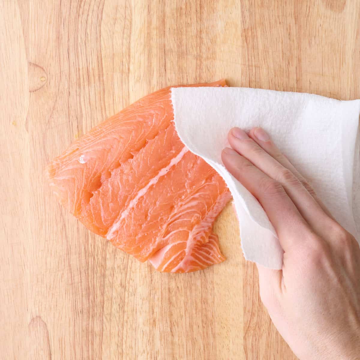Patting salmon fillet dry with paper towel.