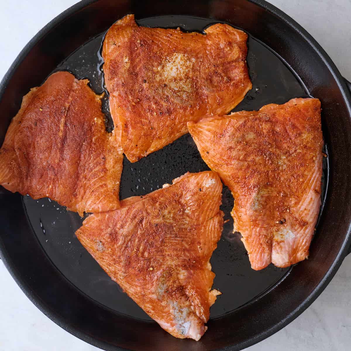 Seasoned salmon in a skillet before cooking.