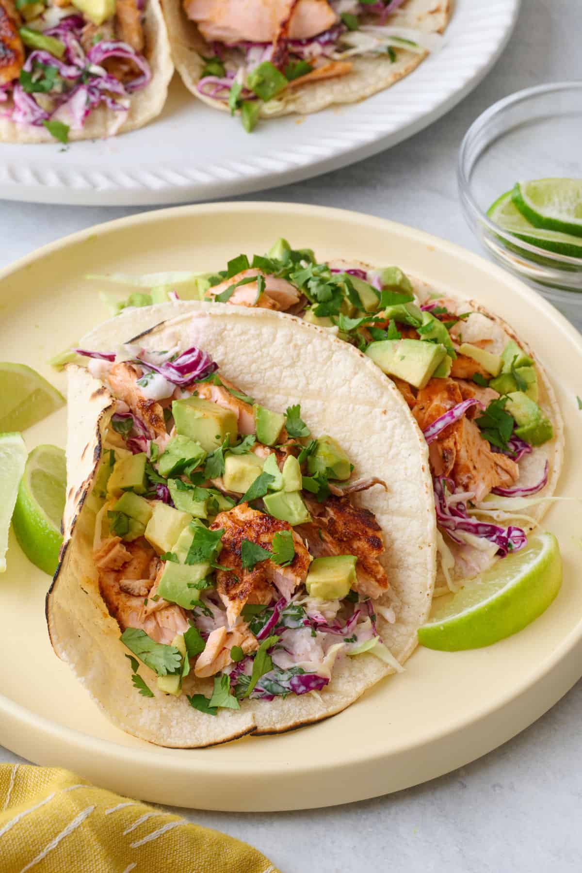 Two assembled, open faced salmon tacos on a small plate with platter nearby.