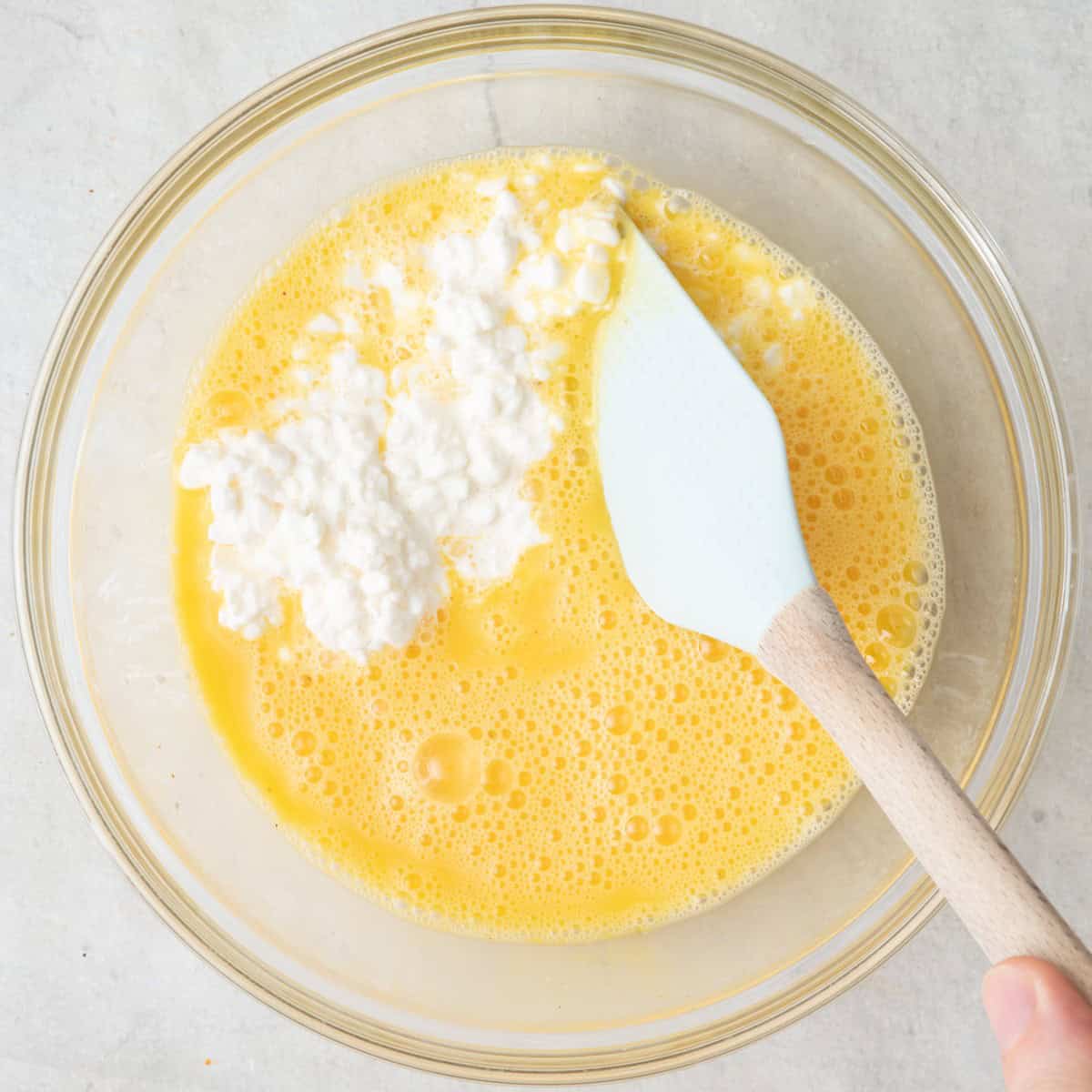 Mixing cottage cheese into eggs in bowl.