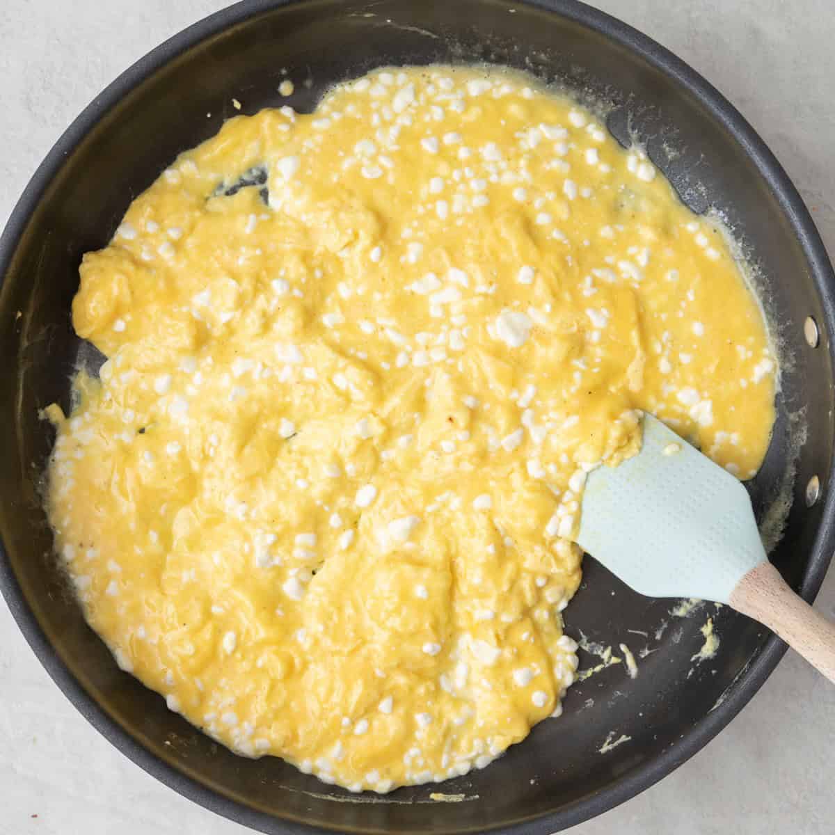 Spatula pushed cooked eggs from edge toward less cooked eggs in center.