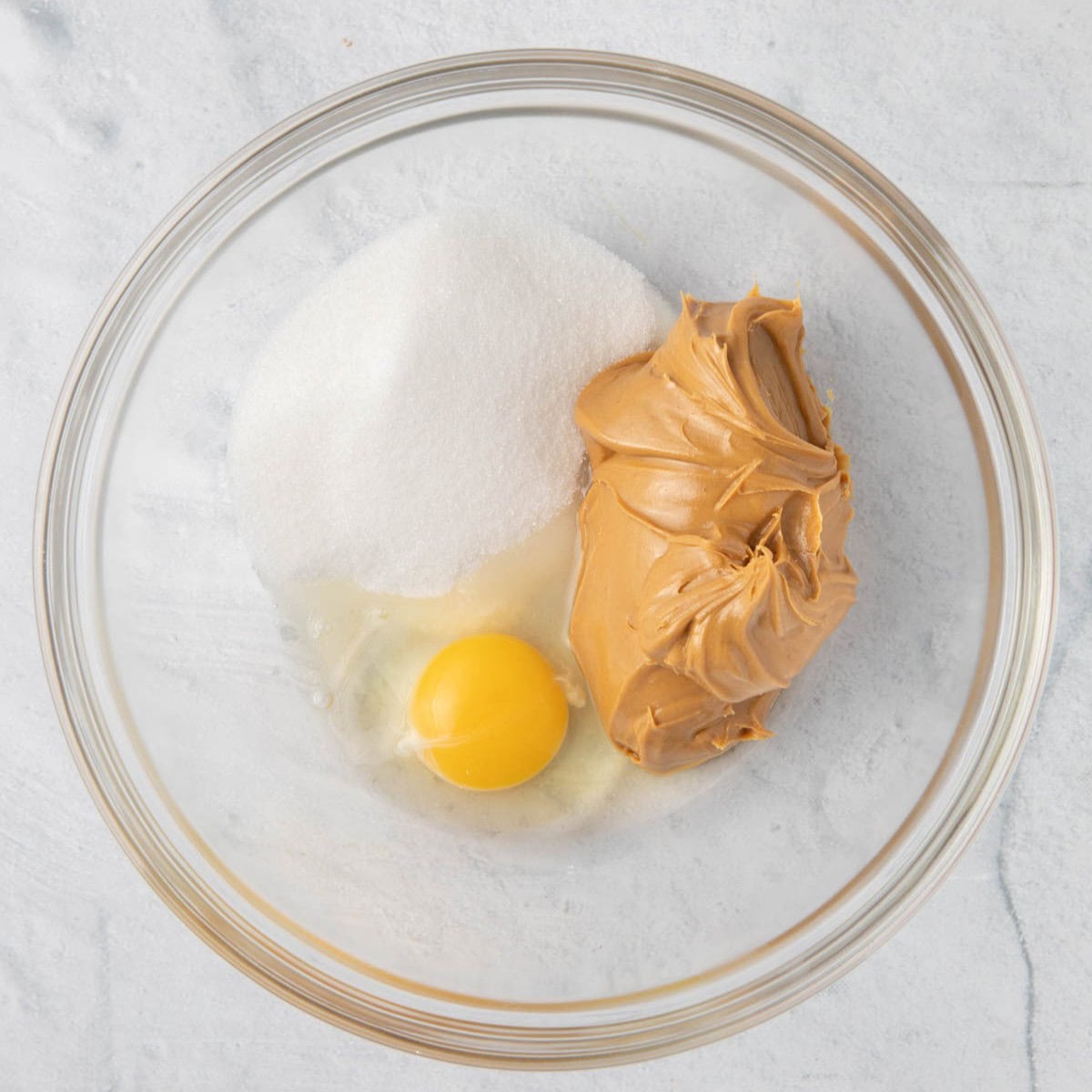 Peanut butter, sugar, and egg in a bowl before mixing.