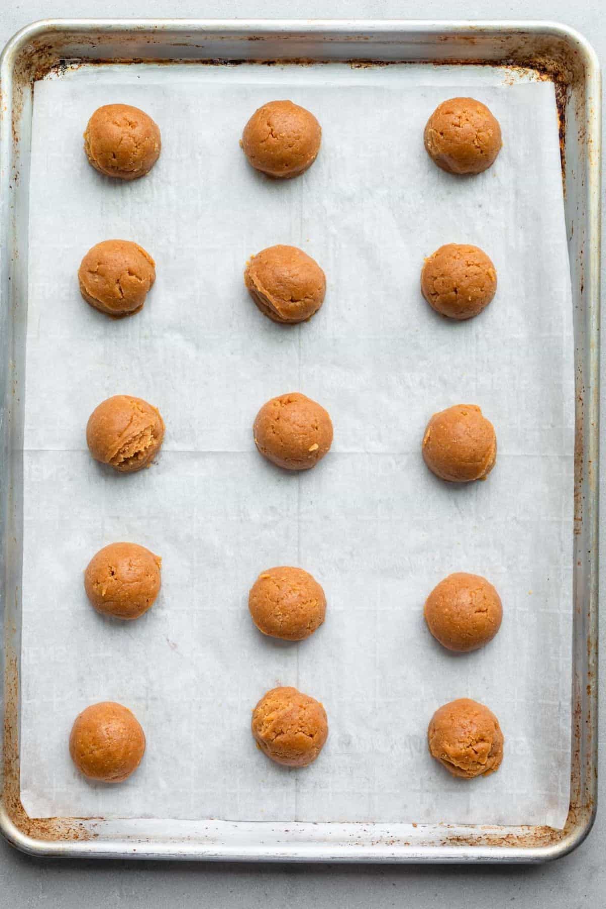 Cookie dough balls on a parchment lined baking sheet.
