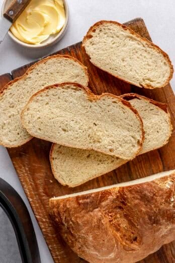 Homemade air fryer bread on a cutting board with a few slices cut and stacked on each other with air fry basket nearby.