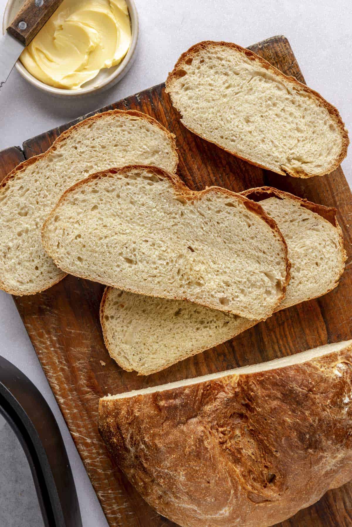 Homemade air fryer bread on a cutting board with a few slices cut and stacked on each other with air fry basket nearby.