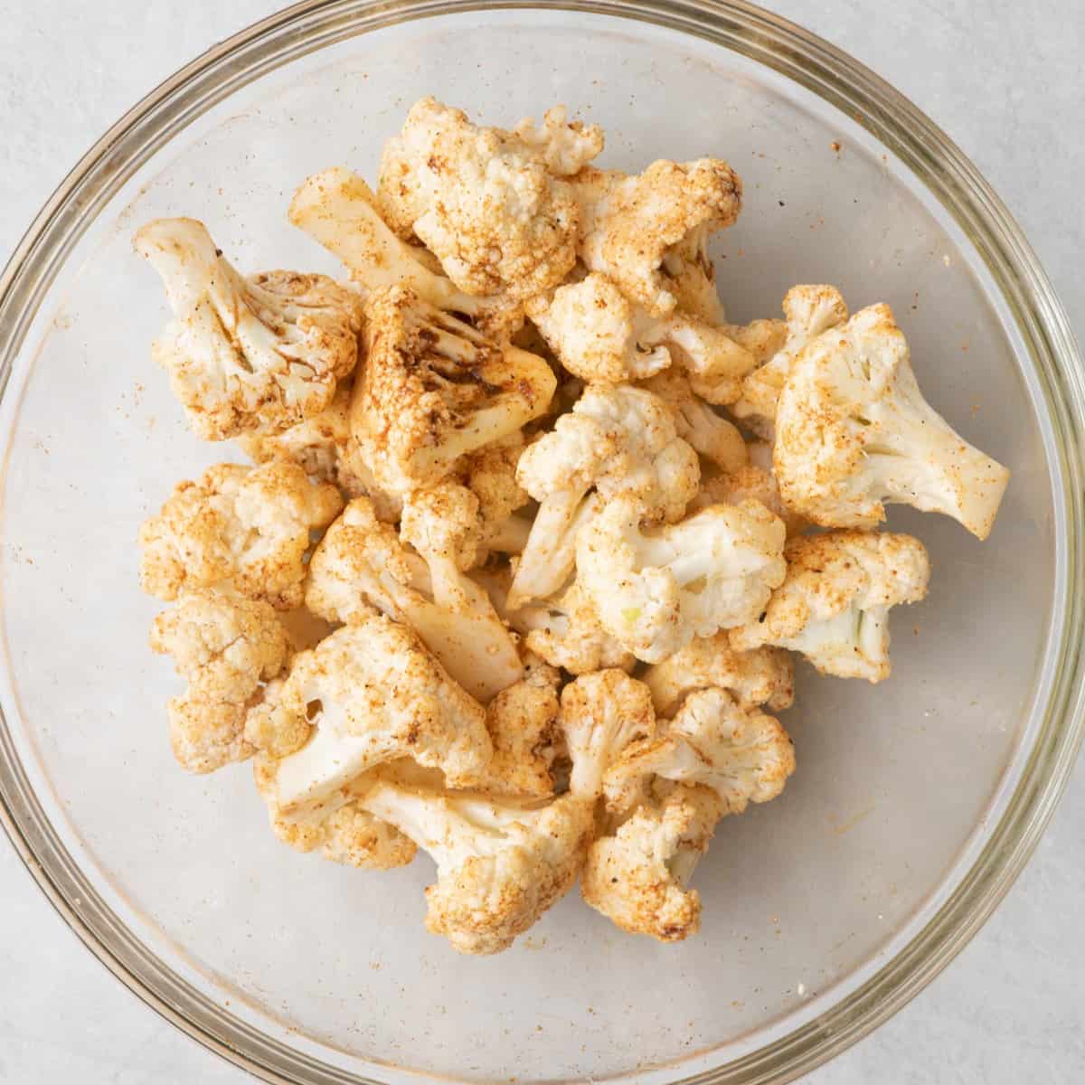 Cauliflower florets in a bowl tossed with olive oil and seasoning.