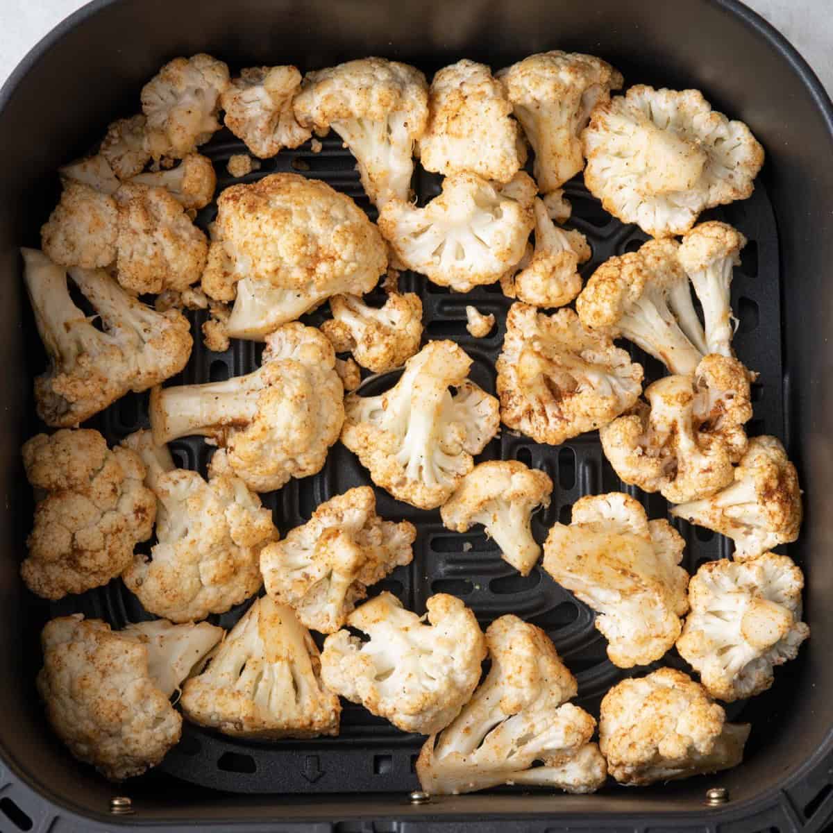 Cauliflower in an air fryer basket arranged in a single layer.