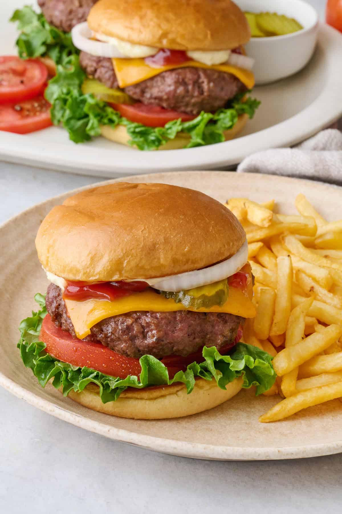 Assemble air fryer burger with cheese on a plate with fries, with platter of more cheeseburgers nearby.