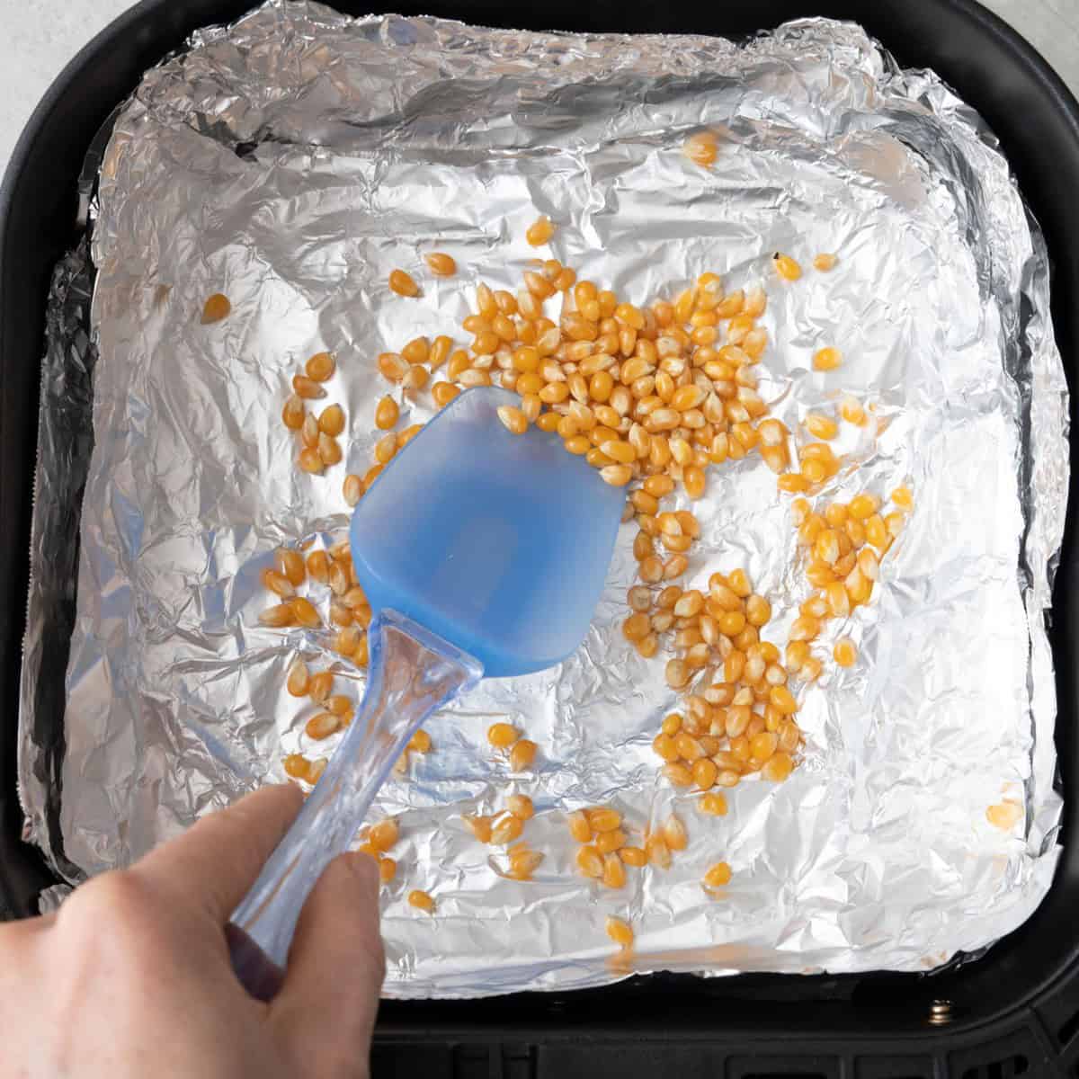 Spoon tossing to combine kernels and oil.