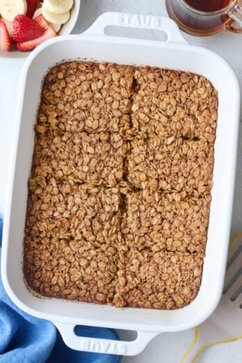 Baked oatmeal in baking dish cut into 8 pieces, and serving spatula nearby.