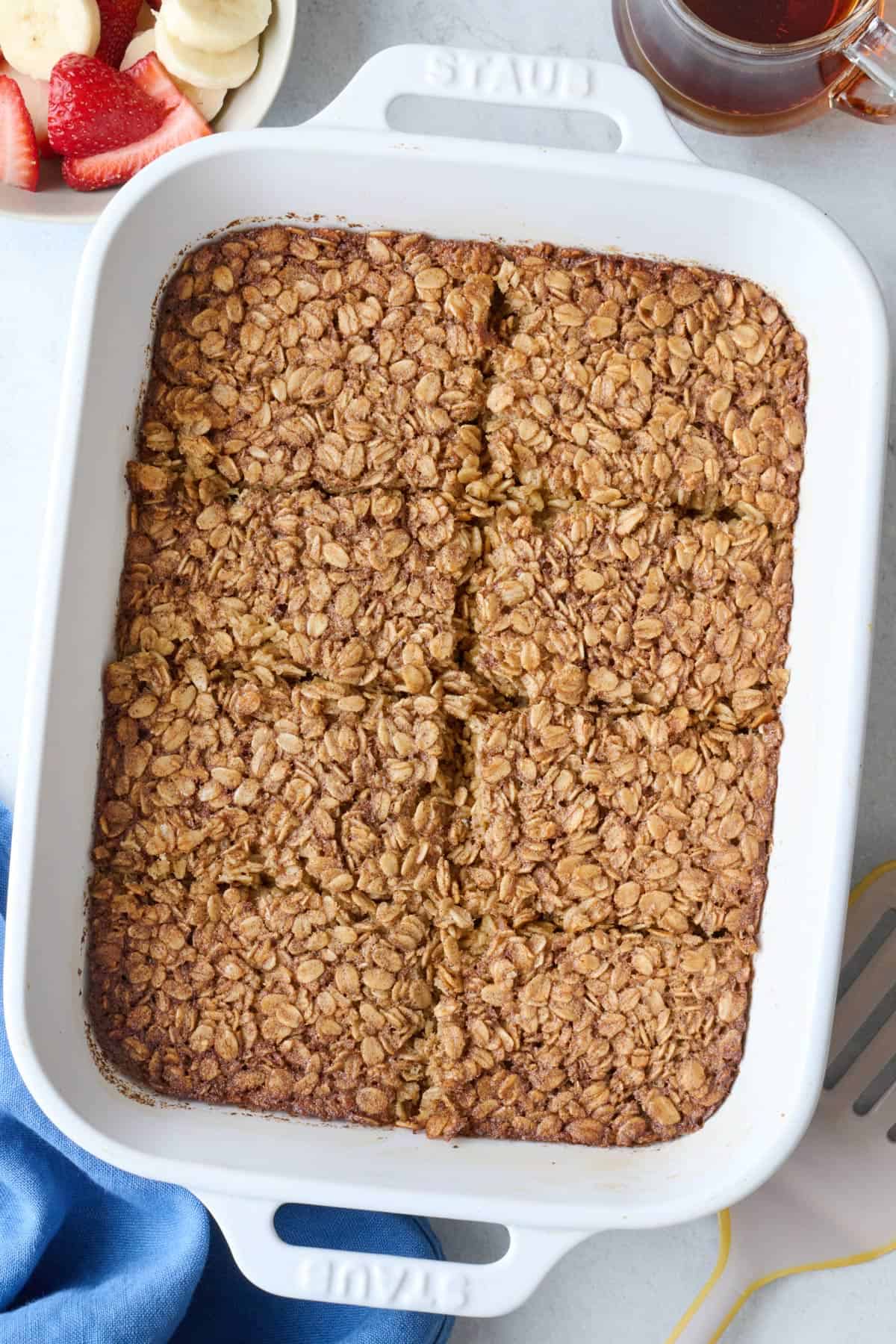 Baked oatmeal in baking dish cut into 8 pieces, and serving spatula nearby.