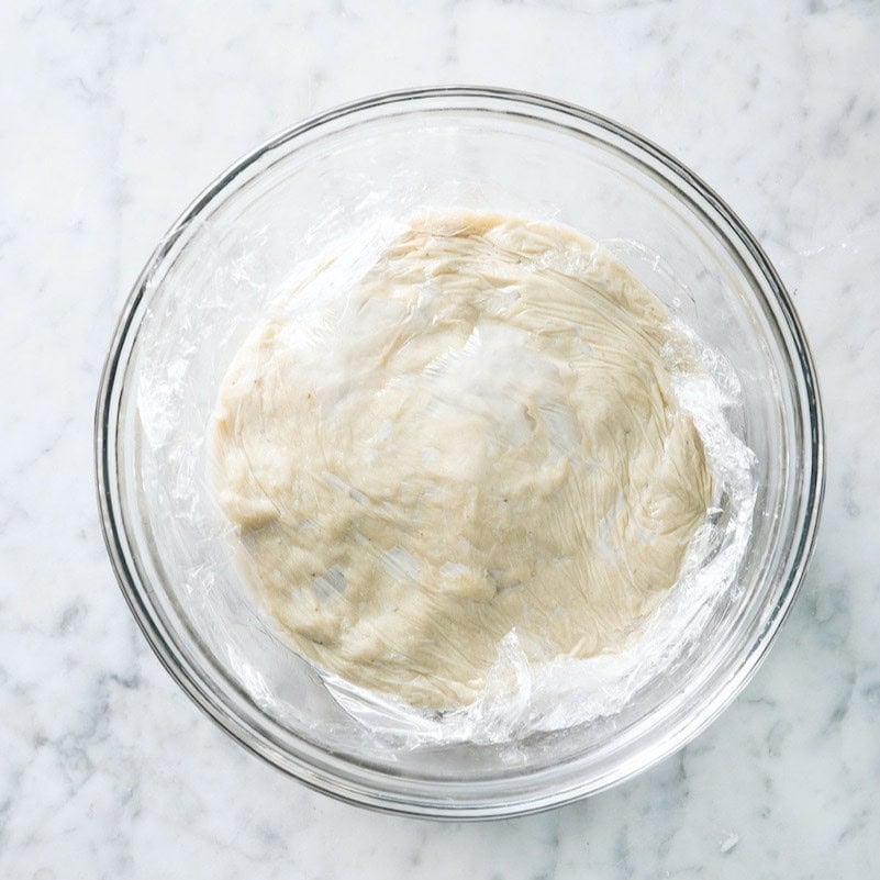 Recipe in a bowl with plastic wrap pressed onto surface.
