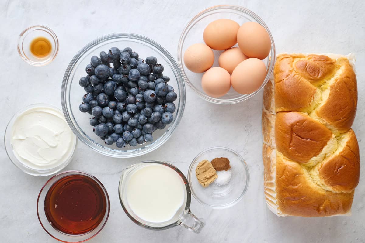 Ingredients for recipe: vanilla, yogurt, blueberry, maple syrup, milk, spices, eggs, and loaf of bread.