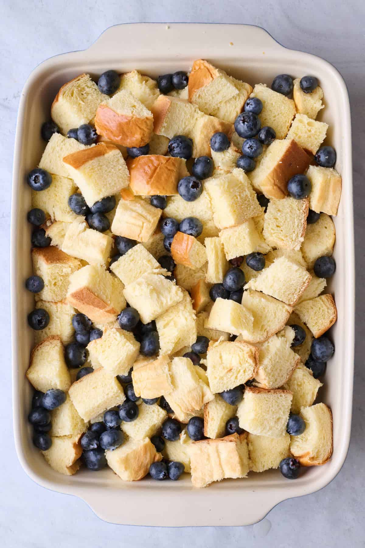 Cubed bread and blueberries in a greased baking dish.