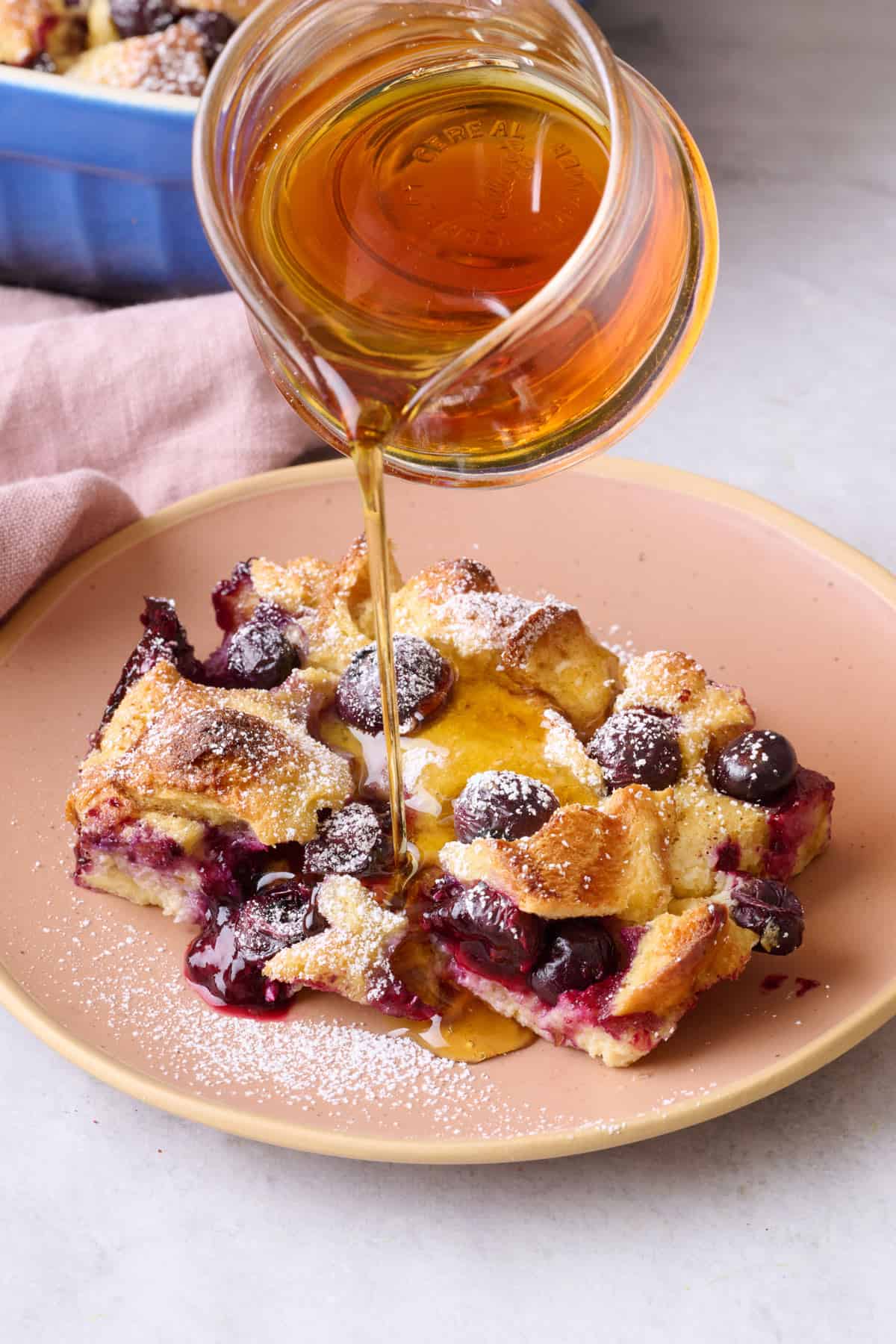 Serving of blueberry french toast bake on a plate with maple syrup being poured over.