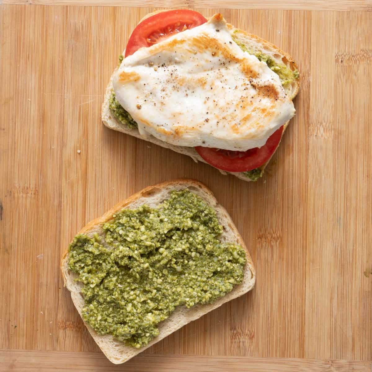 Tomato slices and cooked chicken breast added to one side of bread with pesto.