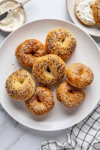 Cottage cheese bagels on a plate with one nearby on a small plate with cream cheese.