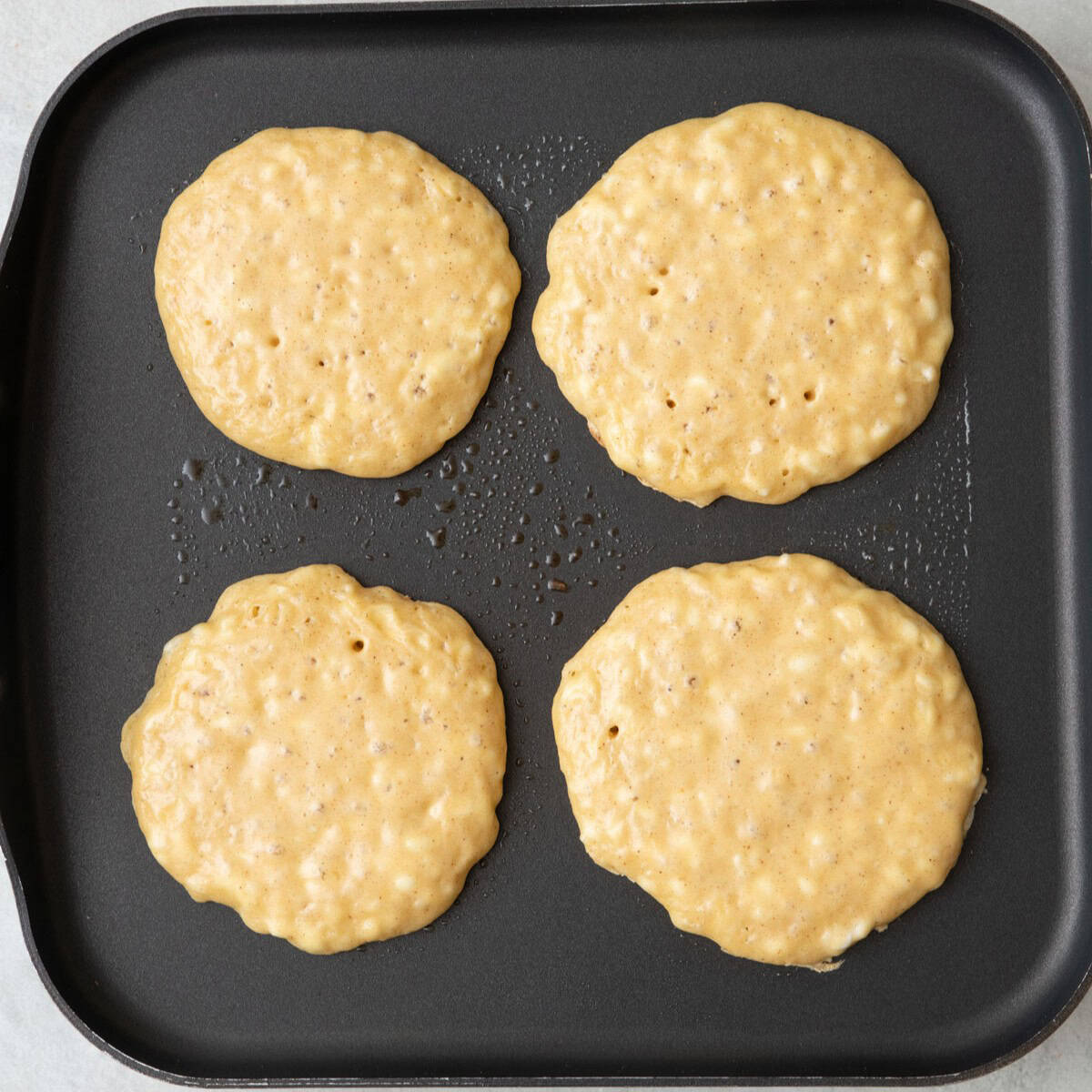 4 pancakes on a griddle before flipping.