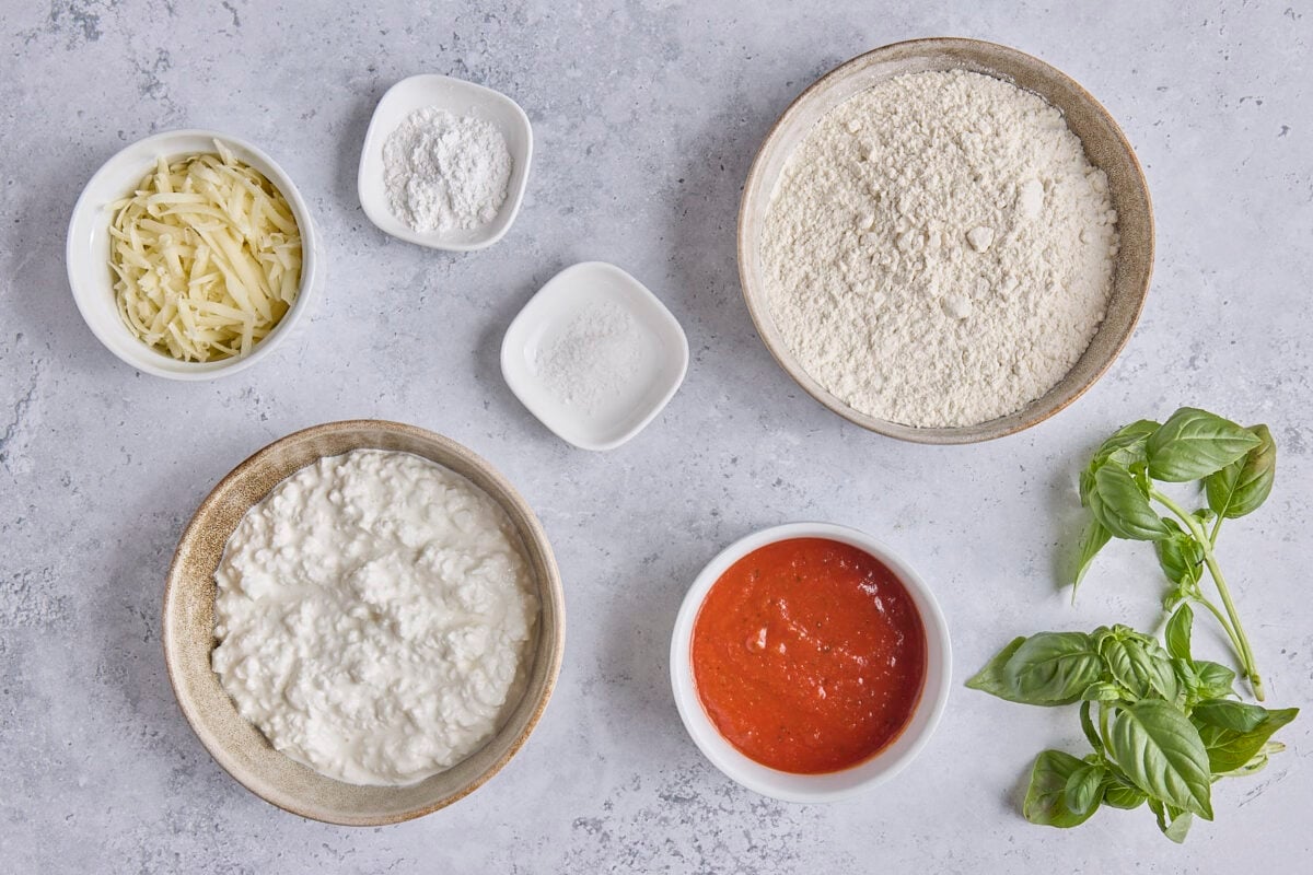 Ingredients for recipe: shredded cheese, cottage cheese, baking powder, salt, marinara, flour, and fresh basil leaves.