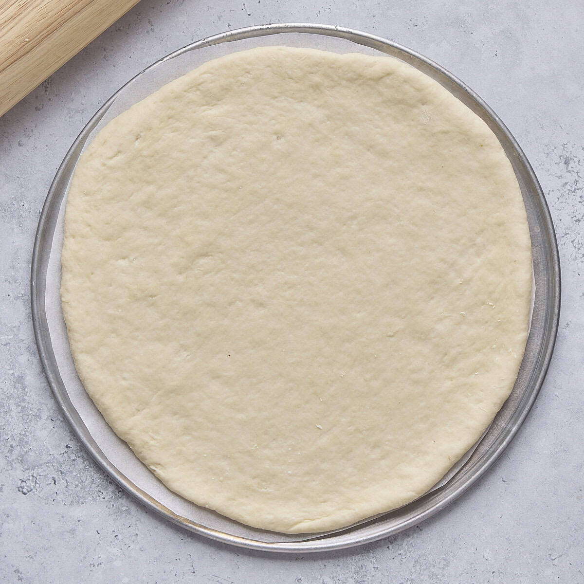 Dough rolled out into a round 9 inch disc on a pizza pan.