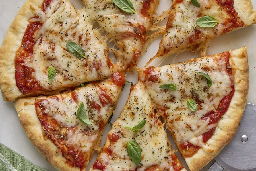 Cottage cheese pizza garnished with basil leaves, cut into 6 large slices with one slice pulled away, pizza cutter nearby.