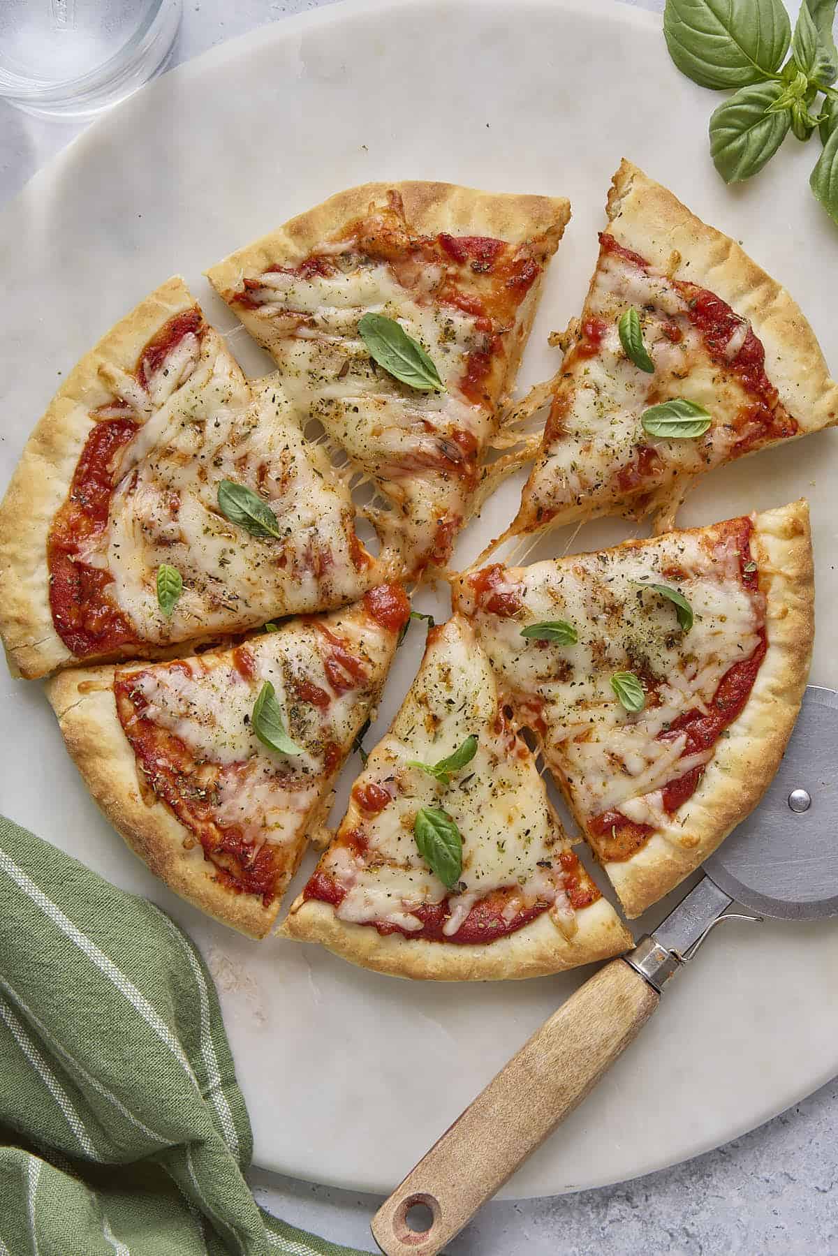 Cottage cheese pizza garnished with basil leaves, cut into 6 large slices with one slice pulled away, pizza cutter nearby.