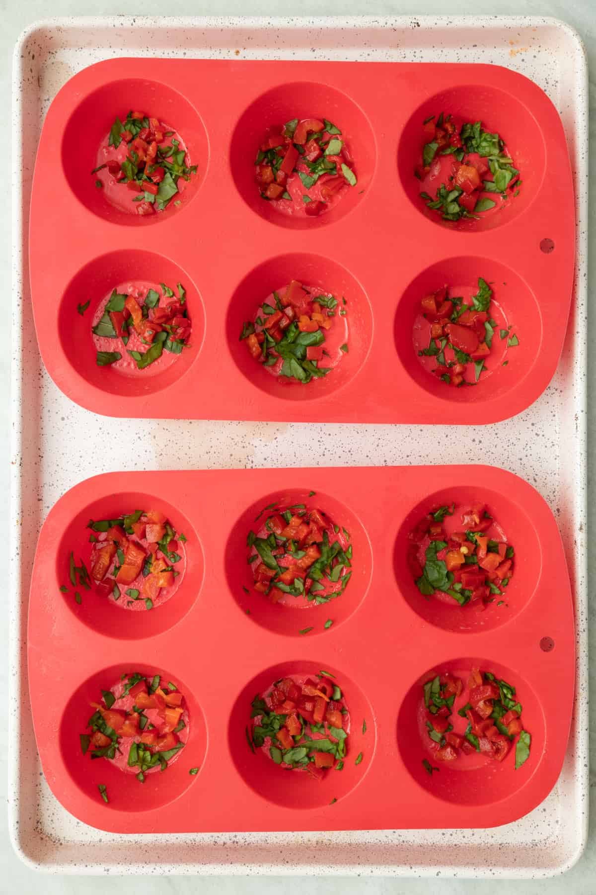 Baking dish with silicone tray inside with the diced peppers and spinach divided into them.