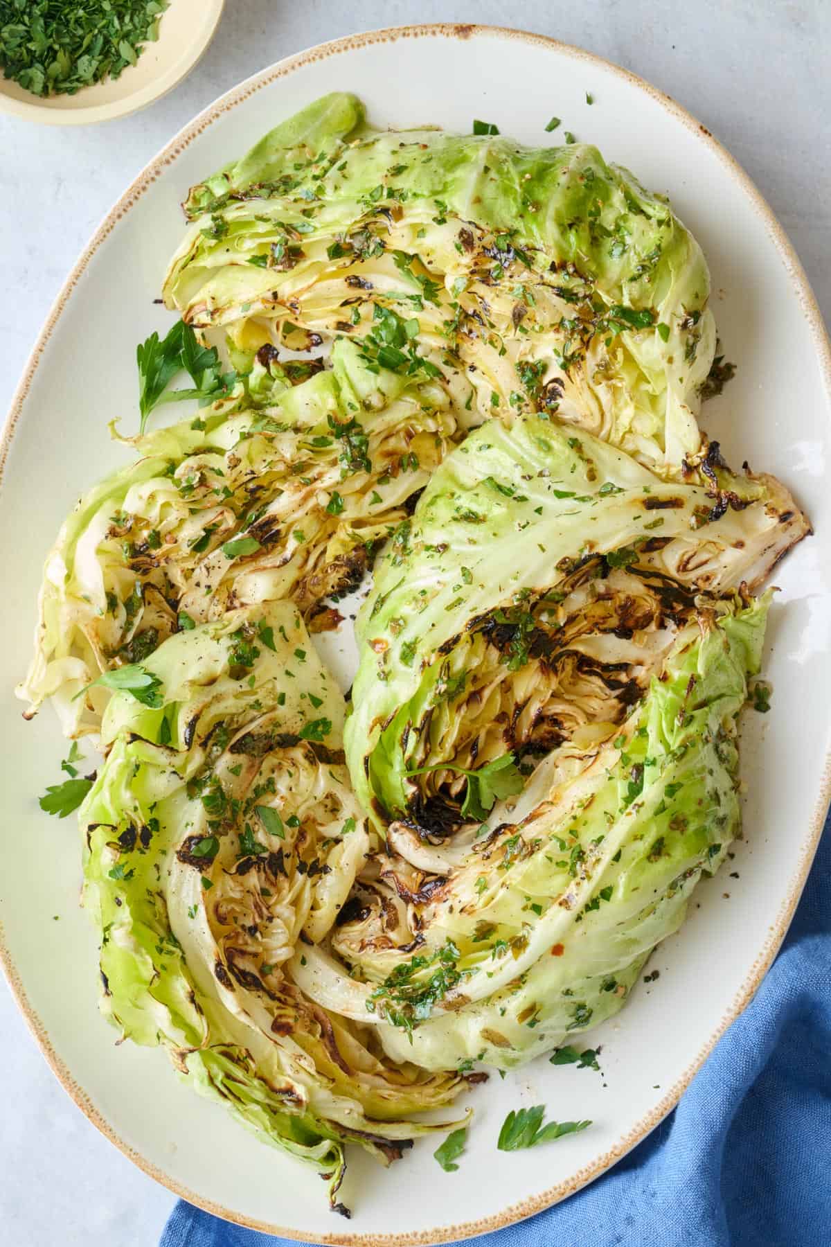 Grilled cabbage topped with chopped fresh herbs on a serving platter.