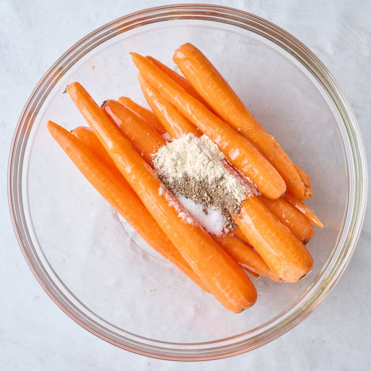 Peeled whole carrots in a bowl with oil, honey, and seasoning.