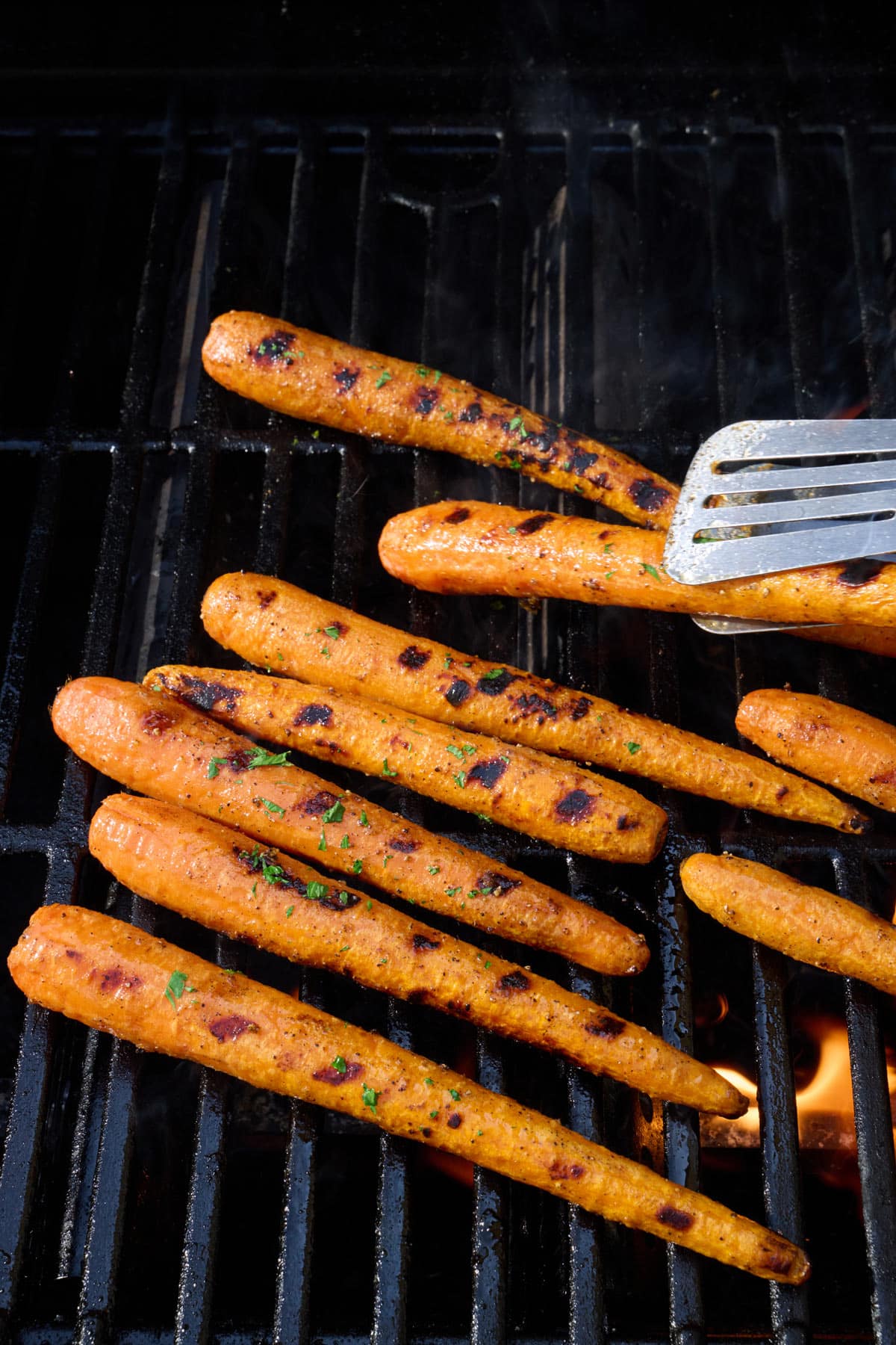 Carrots on grill garnished with fresh parsley with spatula underneath a few.