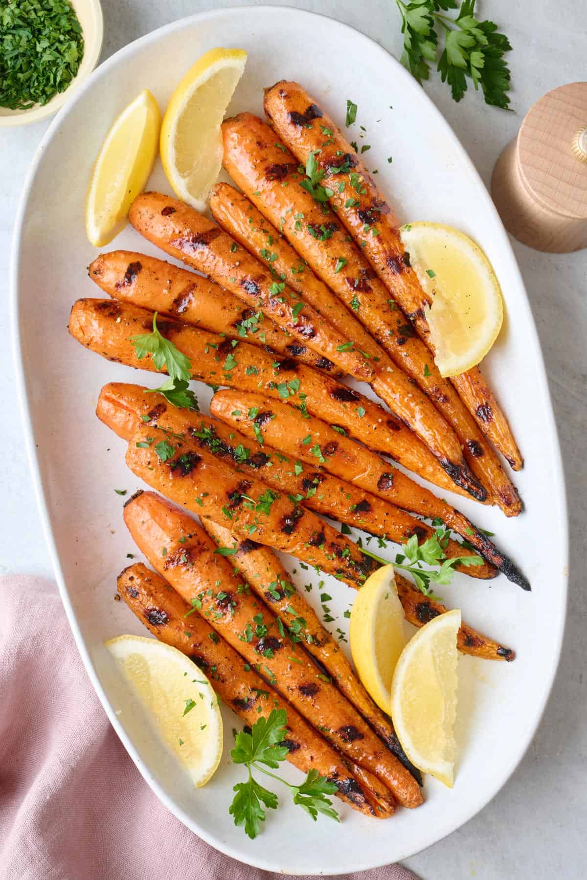 Grilled carrots on a platter, garnished with parsley and lemon wedges.