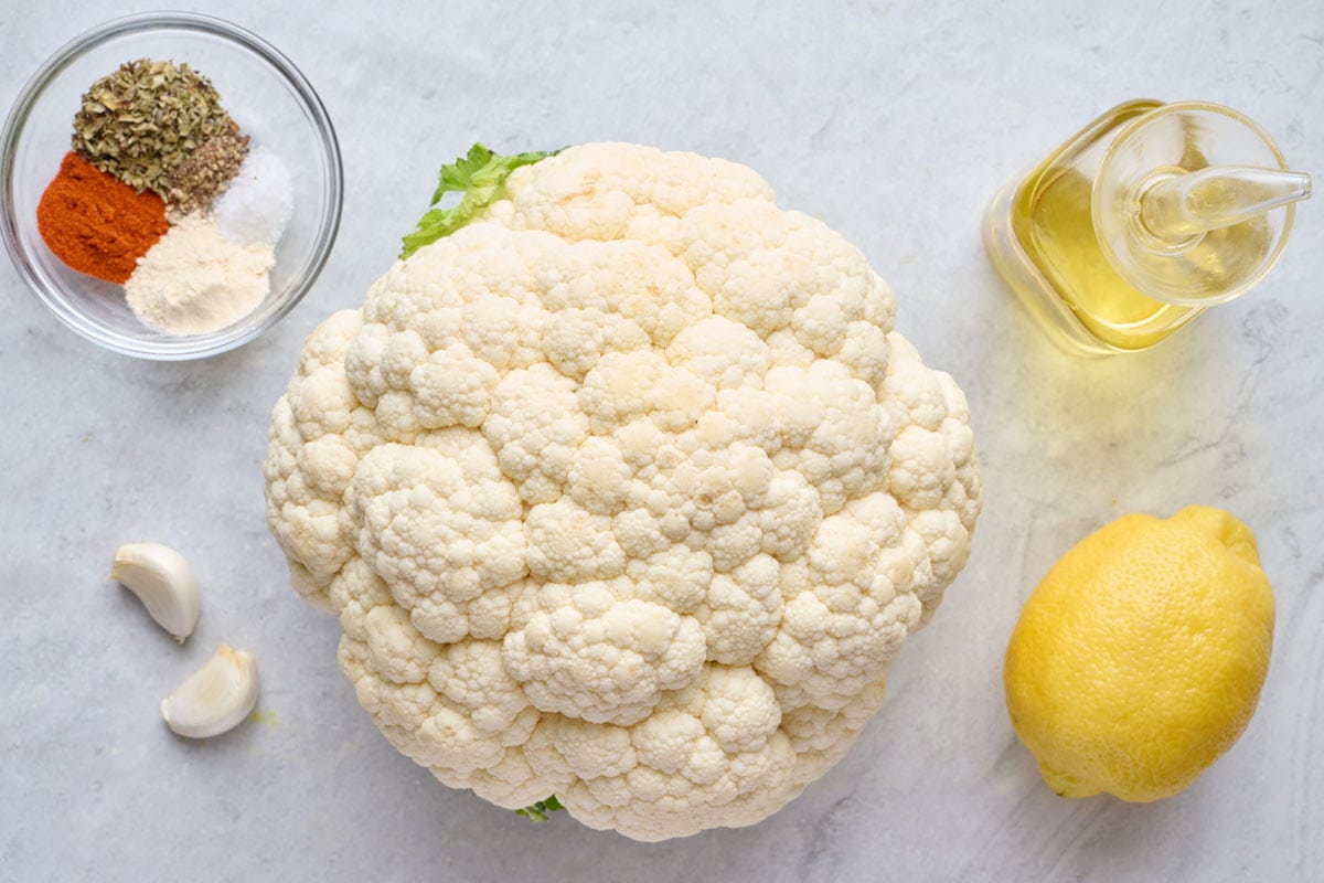 Ingredients for recipe: head of cauliflower, spice blend, garlic cloves, oil, and lemon.