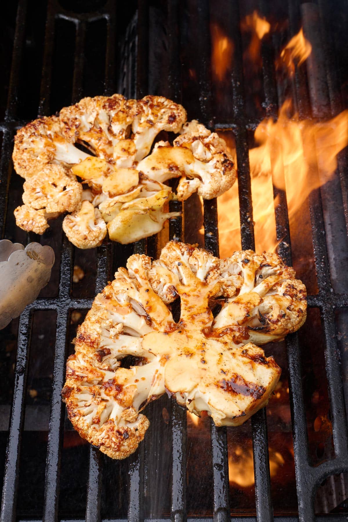 Cauliflower steaks on grill with tongs nearby.