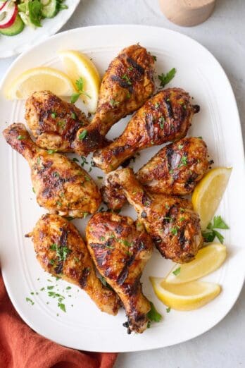 Grilled chicken drumsticks on a platter garnished with parsley and lemon wedges.