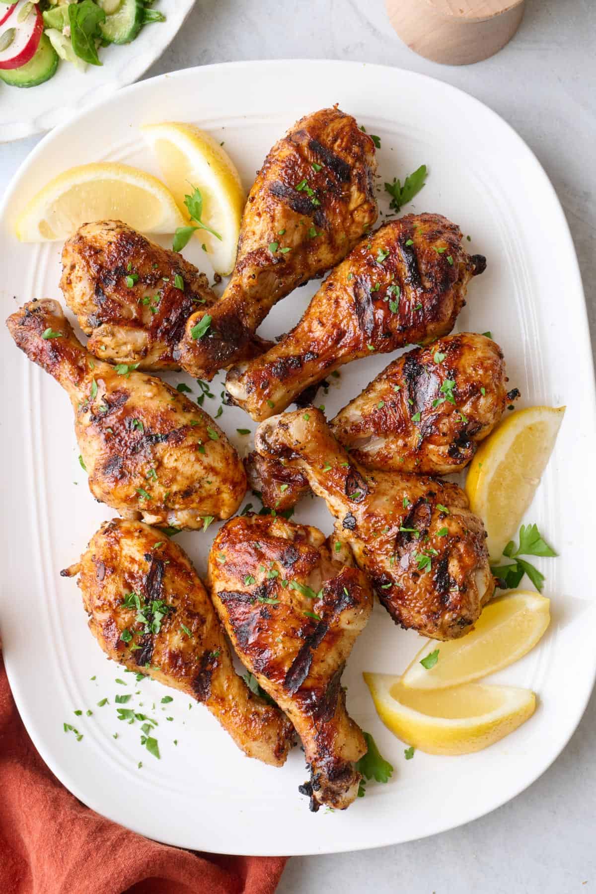 Grilled chicken drumsticks on a platter garnished with parsley and lemon wedges.