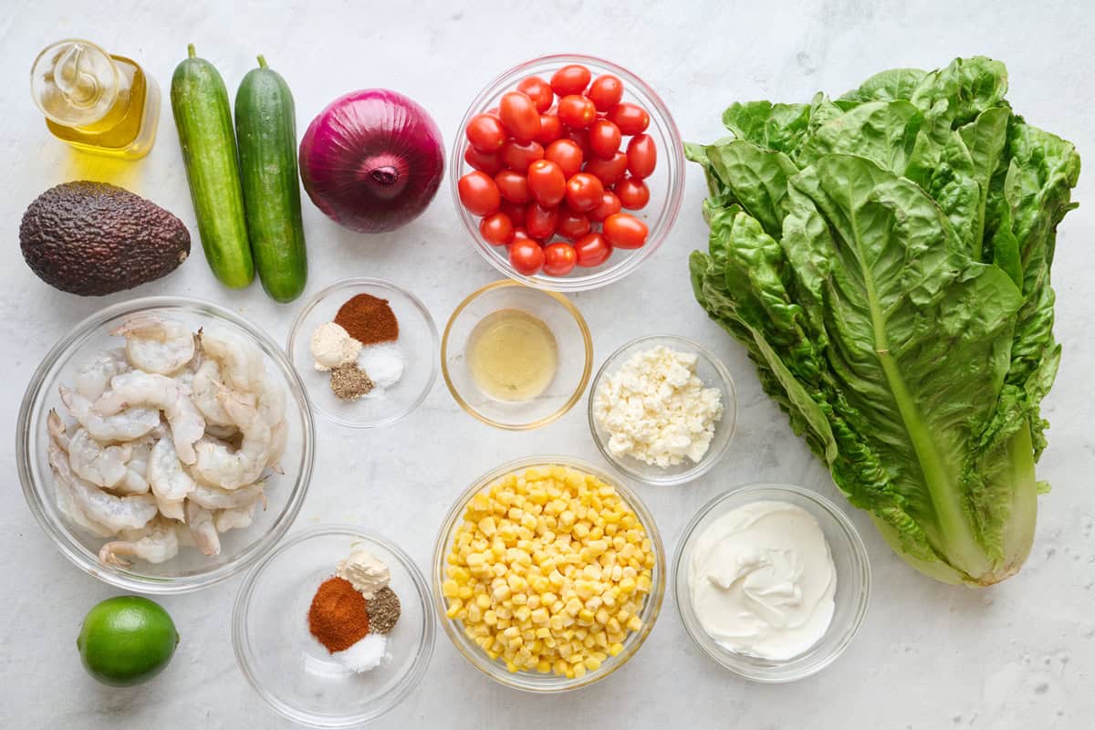 Ingredients for recipe: oil, shrimp, avocado, persian cucumbers, red onion, lime, cherry tomatoes, spices, honey, feta, greek yogurt, and romaine lettuce.