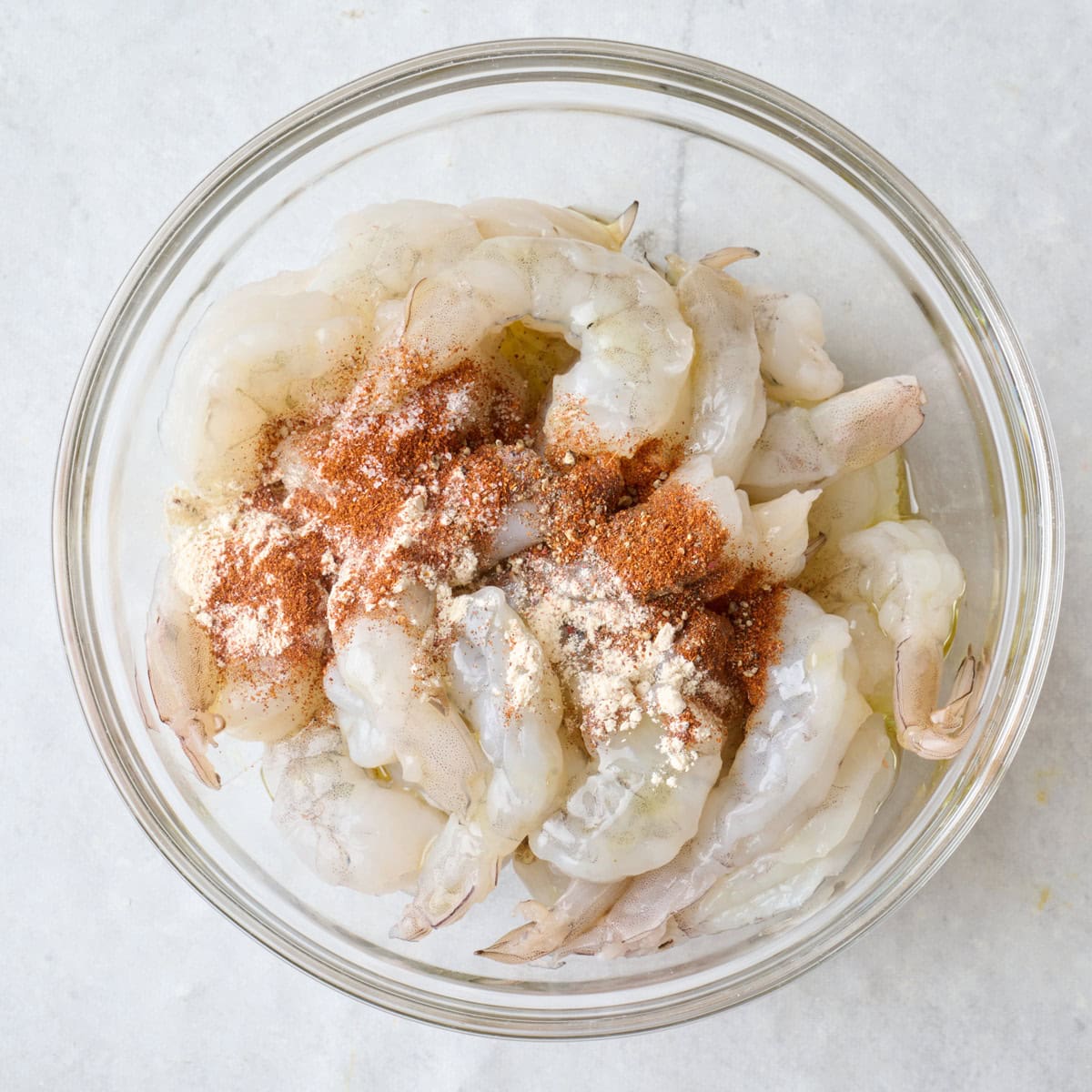 Shrimp in a bowl with oil and seasonings before tossing.