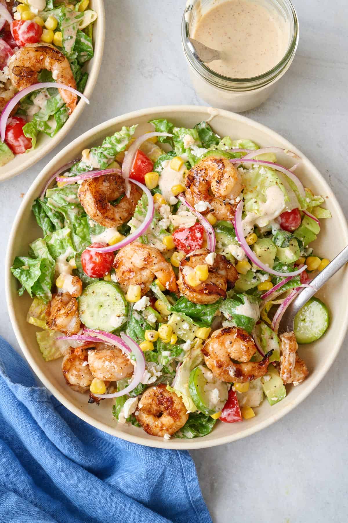 Salad served on two plates, focus on one with jar of dressing nearby with spoon dipped inside.