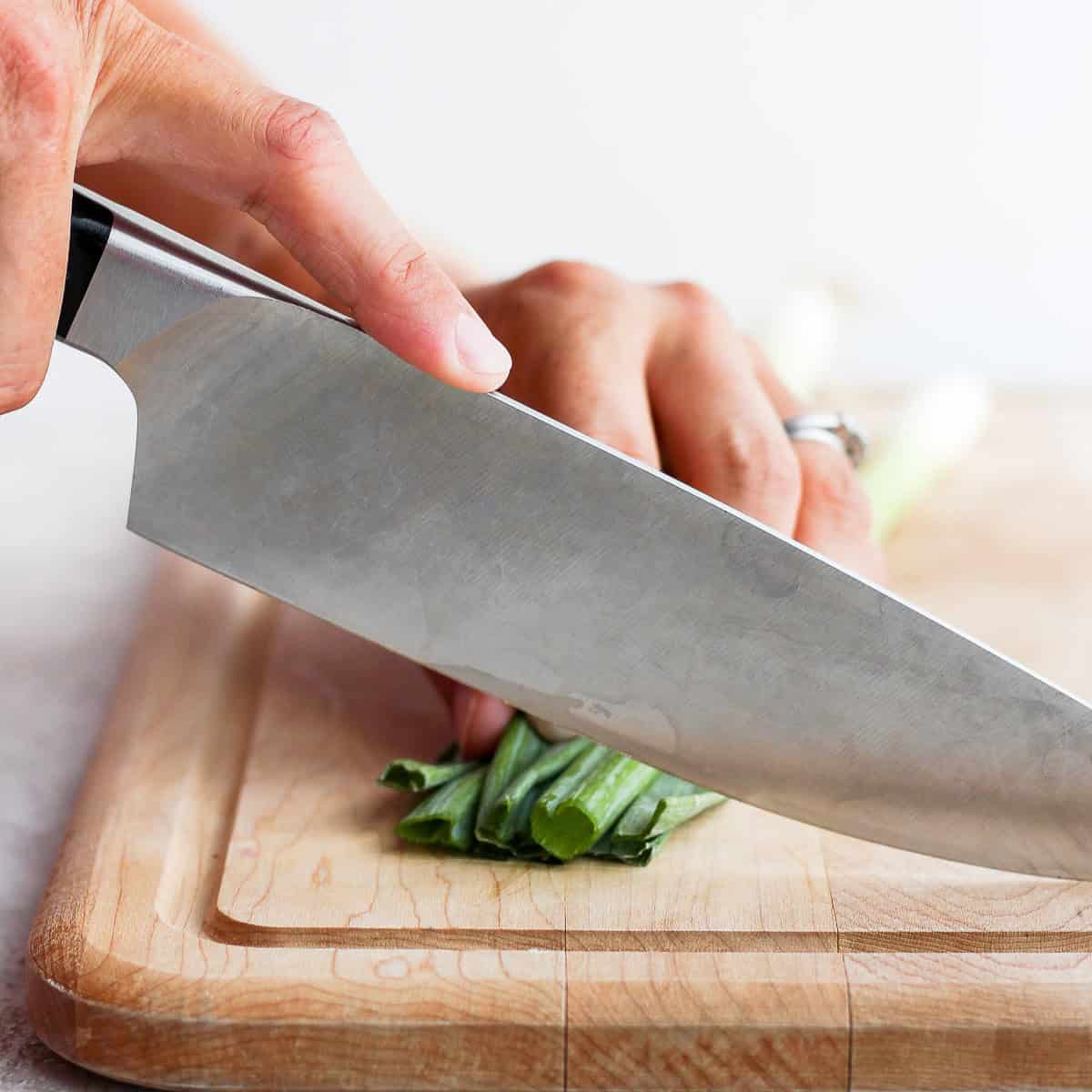 Knife cutting green onions from the top.