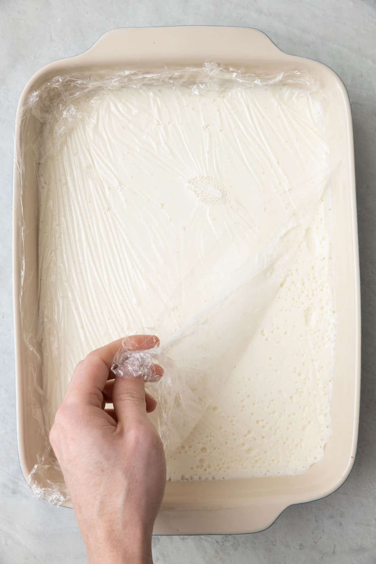 Removing half the plastic wrap after chilled to show firmed ashta.