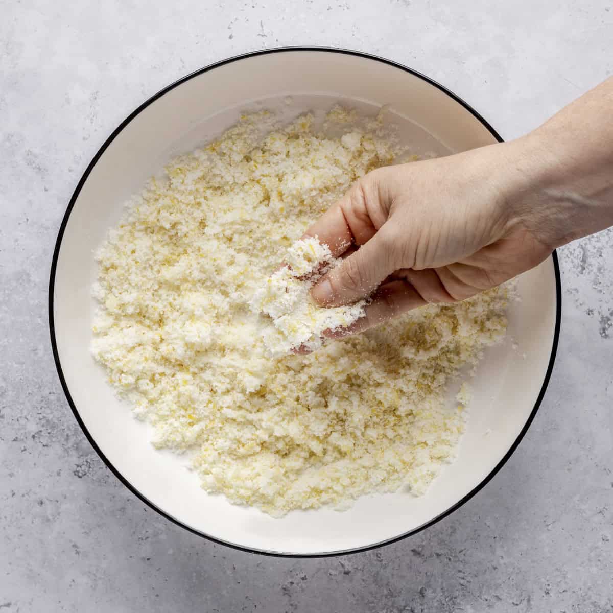 Hands rubbing sugar and lemon zest together after mostly moistened.